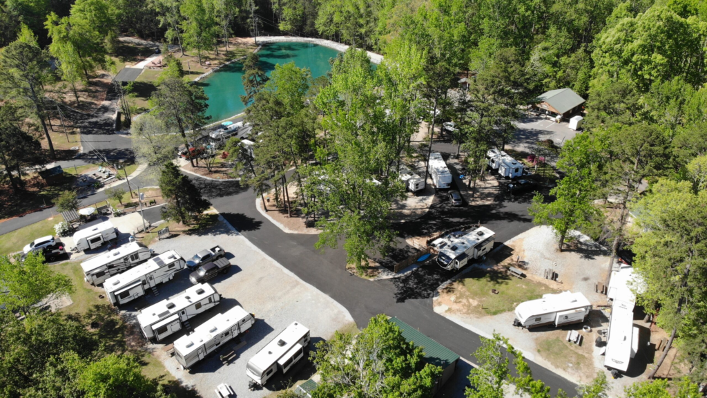 Aerial view of Pine Ridge Campground with RV sites, paved roads, scenic pond, mature trees, and campground amenities.