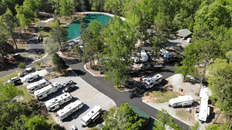 Aerial view of Pine Ridge Campground with RV sites, paved roads, scenic pond, mature trees, and campground amenities.